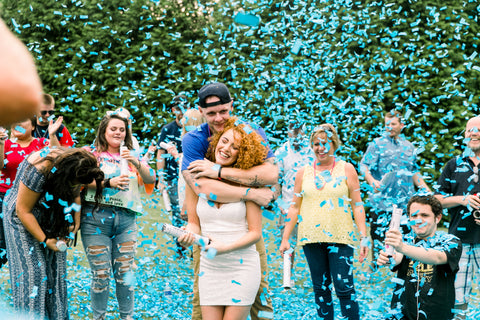 Couple hugging, surrounded by friends and family with blue confetti falling down.