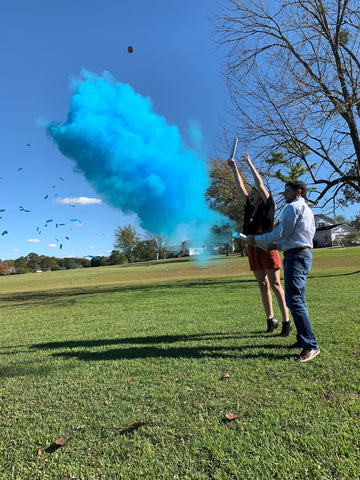 Couple posed outside with blue smoke and confetti.