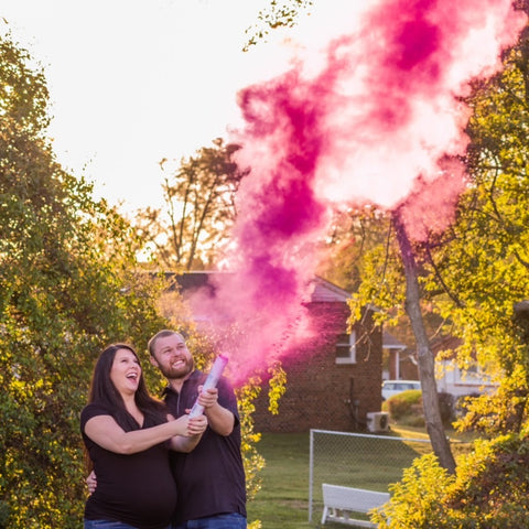 Couple posing with a pink smoke cannon celebrating having a baby girl.