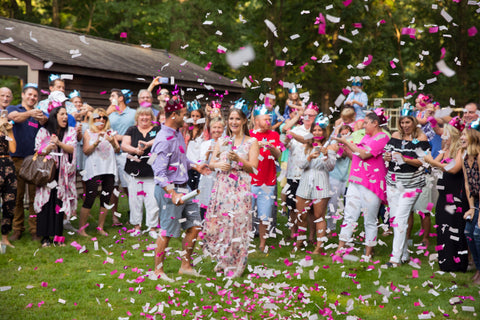 Couple posing outside, surrounded by friends and family with pink confetti all around.