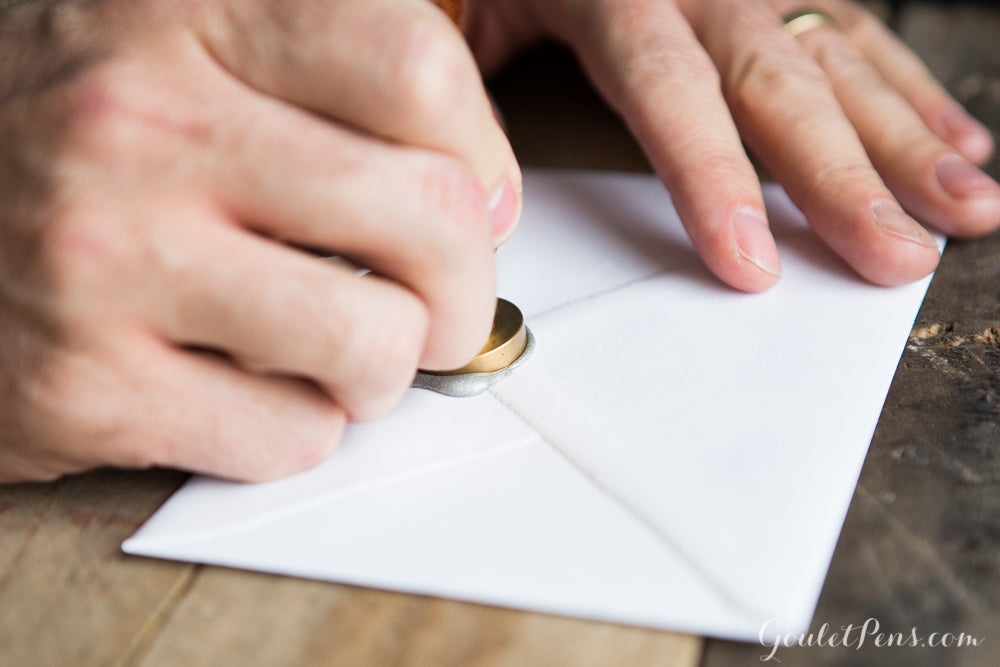 A hand creating a wax seal on an envelope
