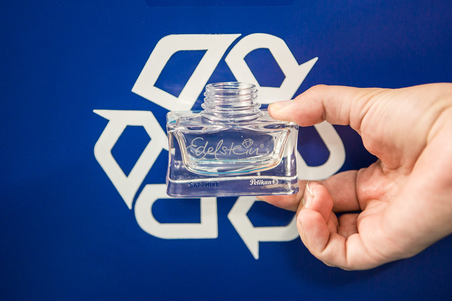 hand holding an empty ink bottle in front of a blue recycling sign