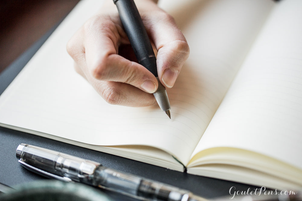 hand holding a LAMY 2000 fountain pen over a white notebook