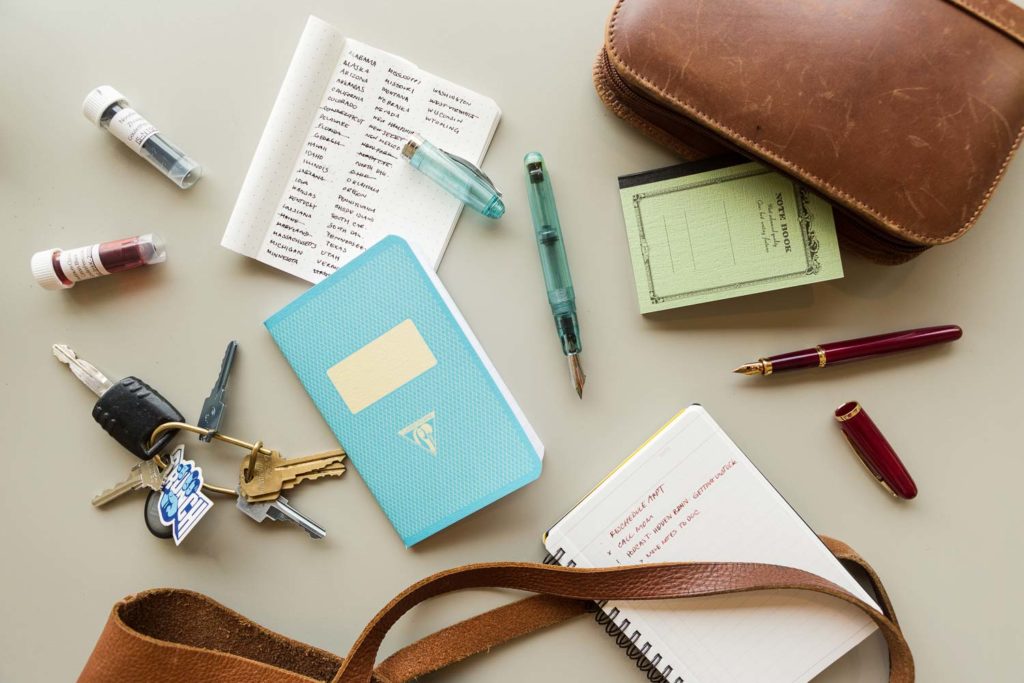 A blue Clairefontaine notebook with a set of keys and purse straps on a table