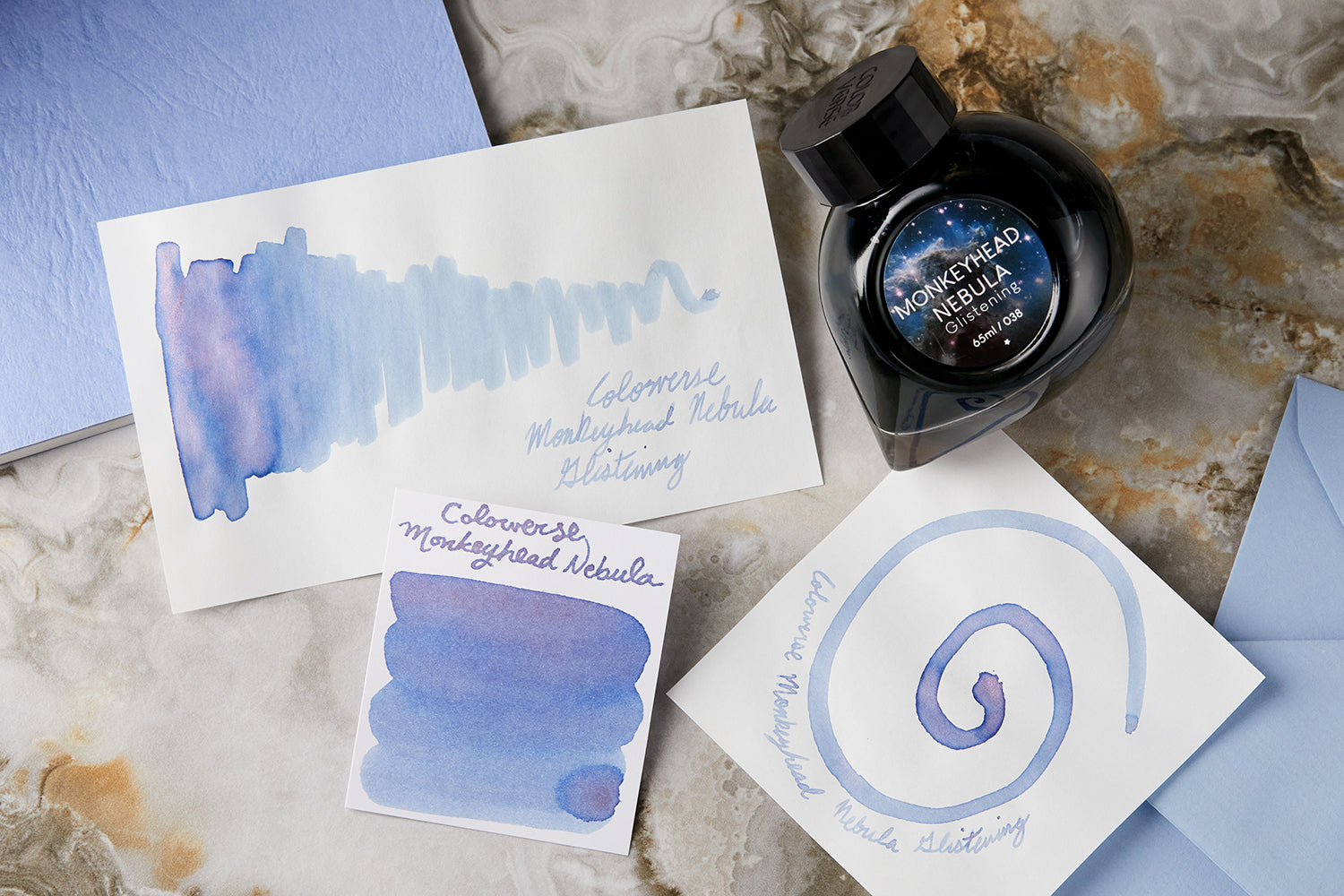 Colorverse Monkeyhead Nebula Glistening fountain pen ink bottle, writing sample, swab and swatch on white background with purple envelopes