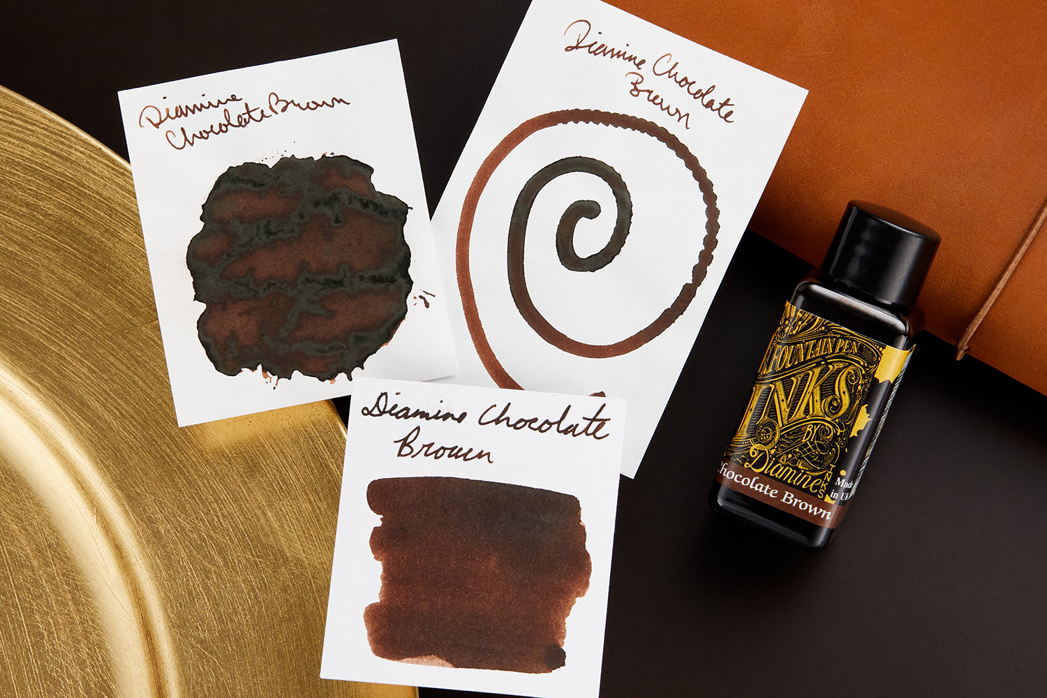 Diamine Chocolate Brown Fountain Pen Ink with ink swab, swatches, writing sample, and bottle on leather desk blotter background.