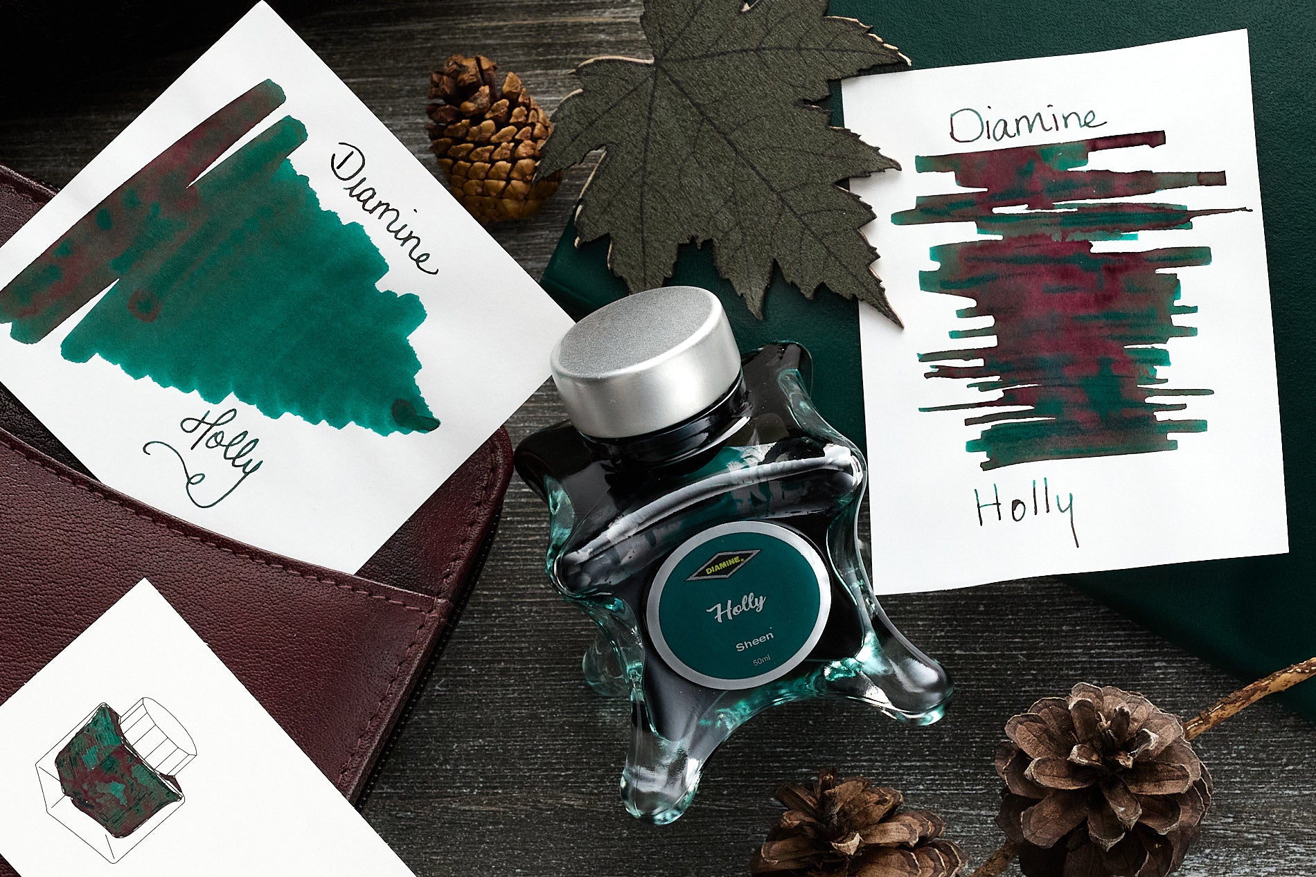 Diamine Holly Fountain Pen Ink writing sample, and swabs, along with the bottle and pinecones on a wooden desk background