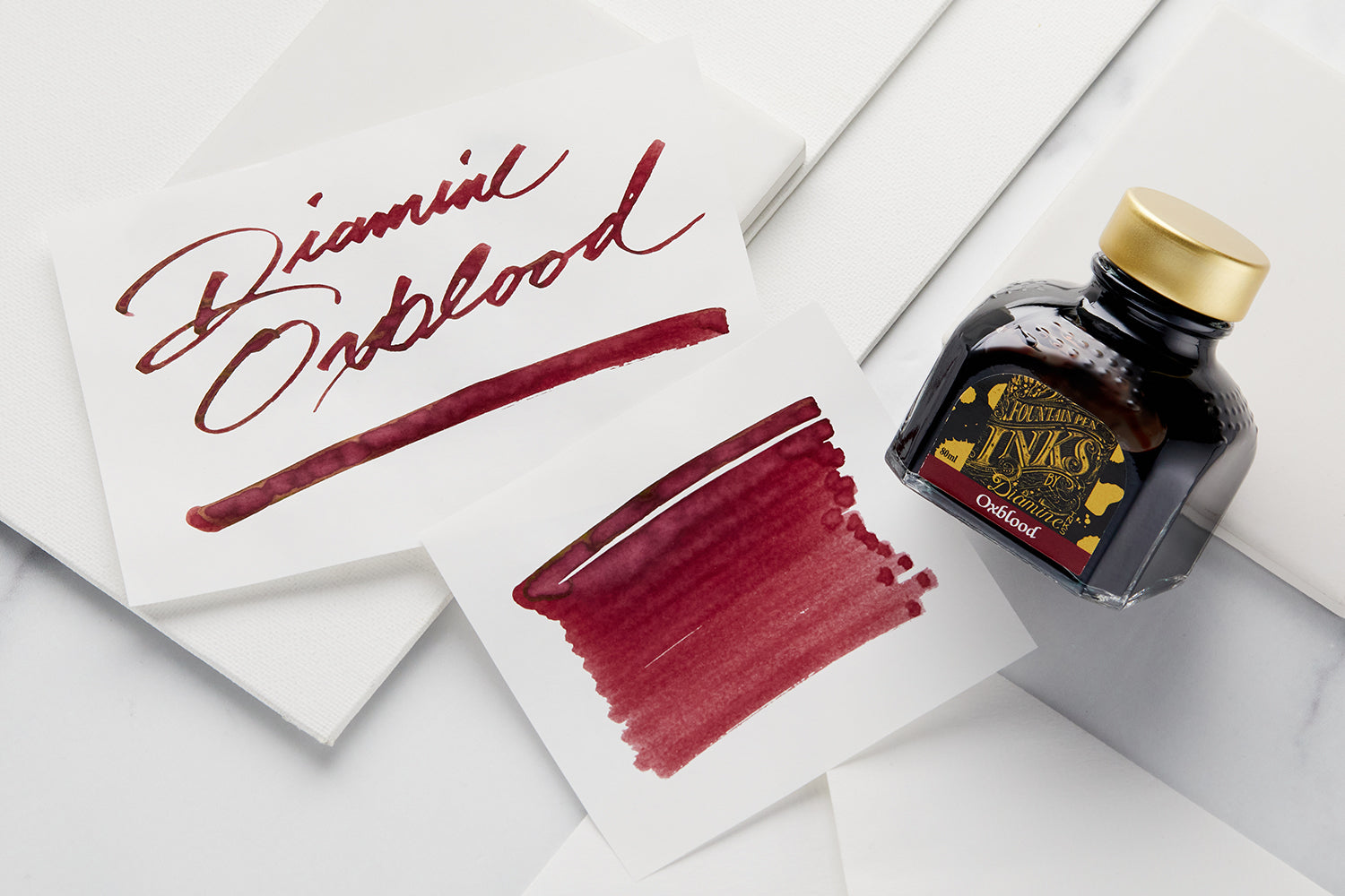 Diamine Oxblood Fountain Pen ink bottle and 2 white cards with text and swab on them respectively. Text reads Diamine Oxblood