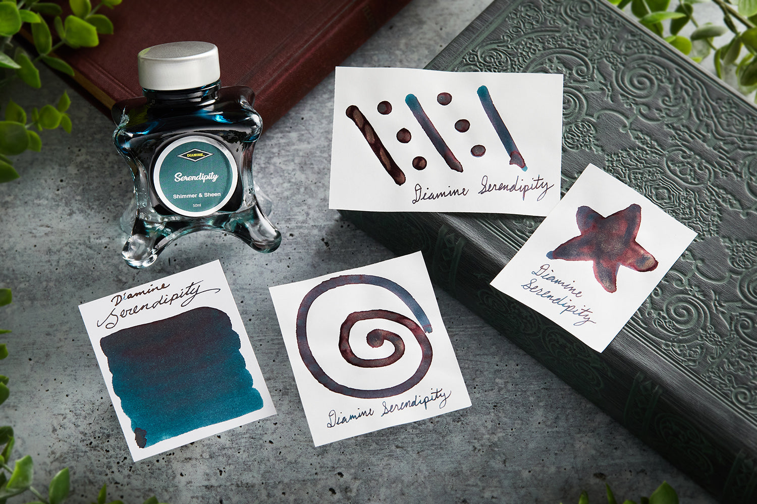 Diamine Serendipity fountain pen ink bottle along with 4 white cards that have ink swabs, symbols, or doodles, with a gray background