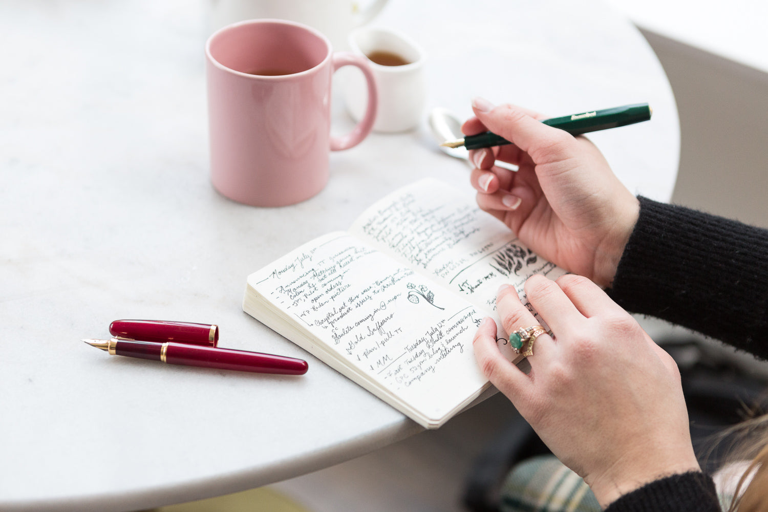 Open notebook with a fountain pen and handwriting and a coffee cup in the background