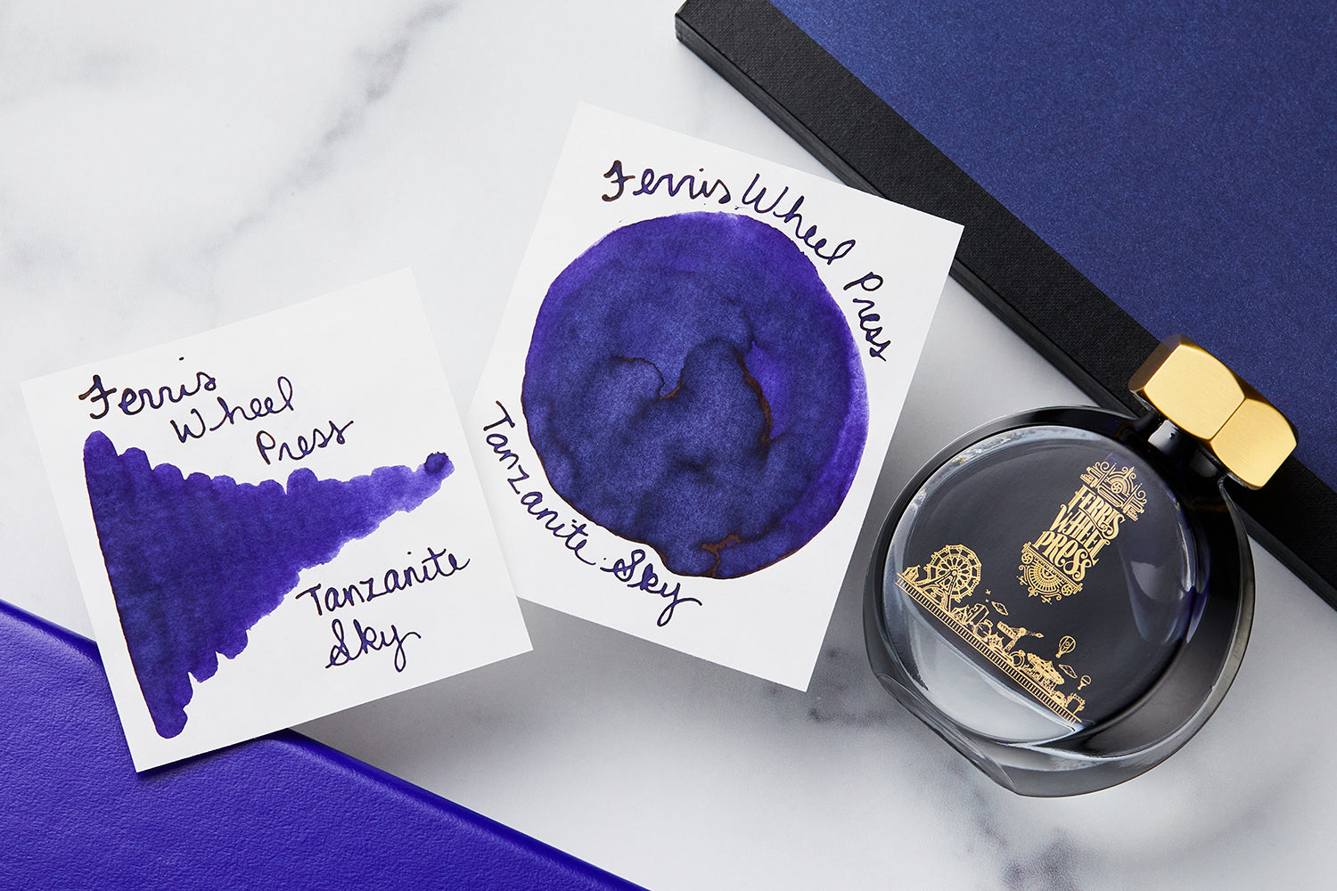 Ferris Wheel Press fountain pen ink bottle with 2 white cards with swatch on them, all on top of a marble table with a purple notebook in the background