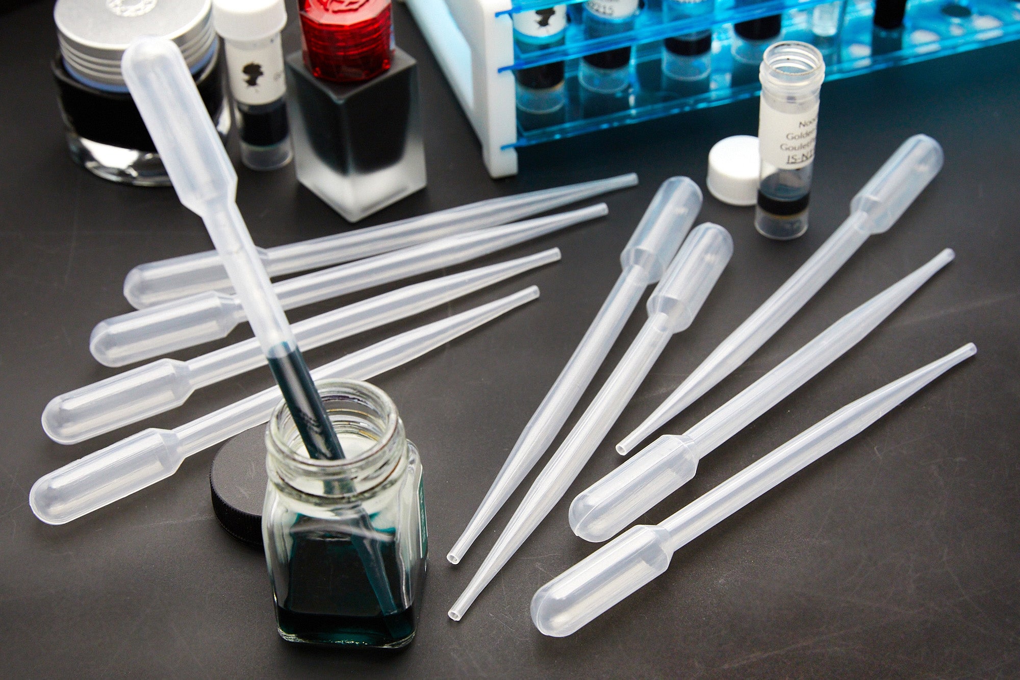 Goulet Transfer Pipettes - one inserted into a bottle of ink, standing upright, the rest empty and on a gray desk background