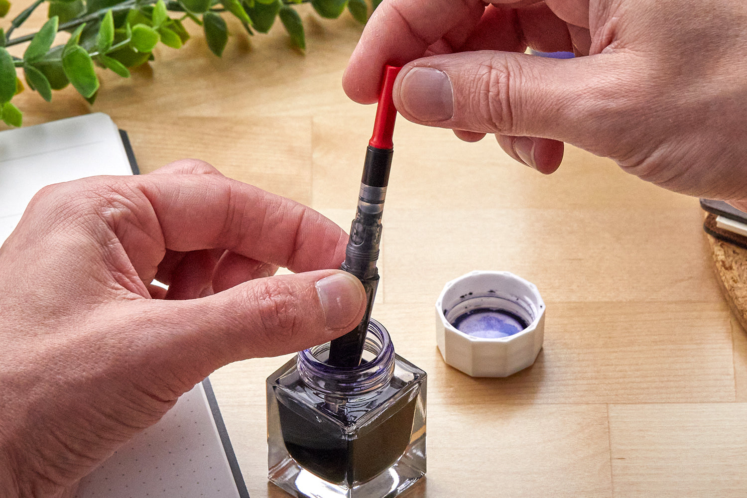Hands filling a LAMY fountain pen with ink from a bottle