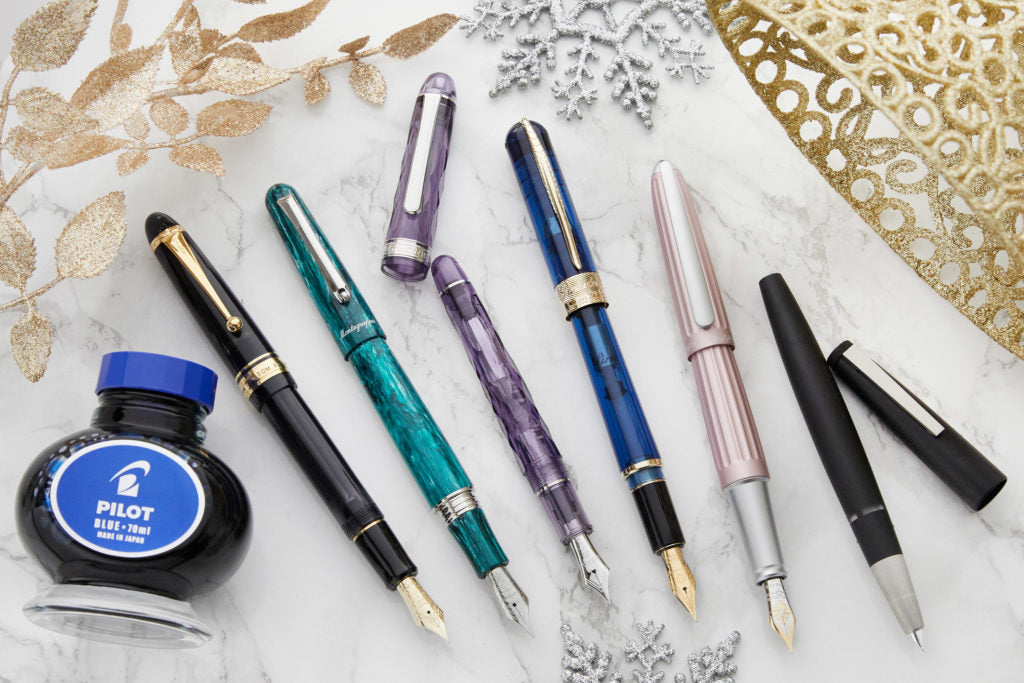Assorted fountain pens uncapped with winter decorations in the background