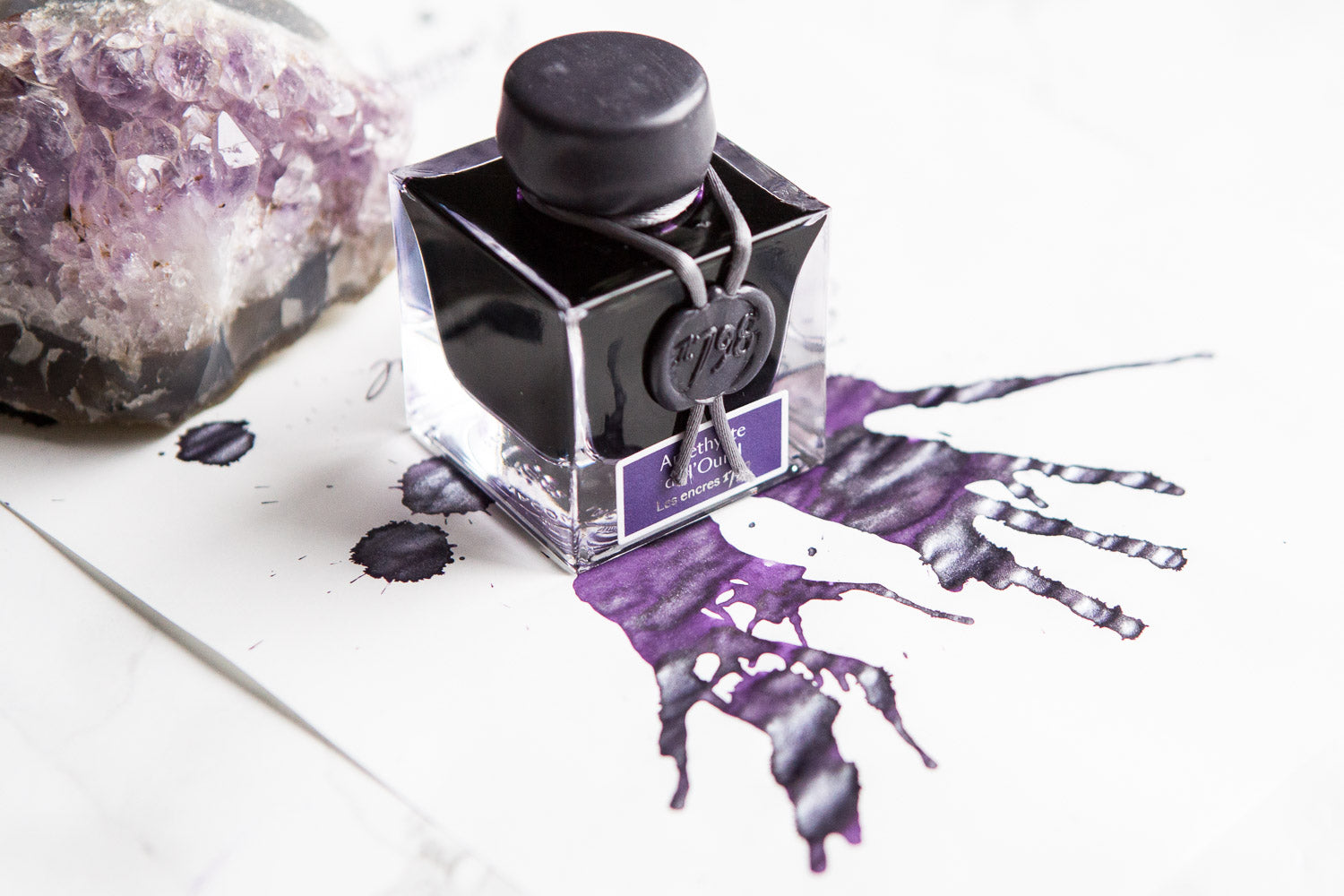 Jacques Herbin Amethyste de l'Oural fountain pen ink bottle with purple ink splatters on white paper