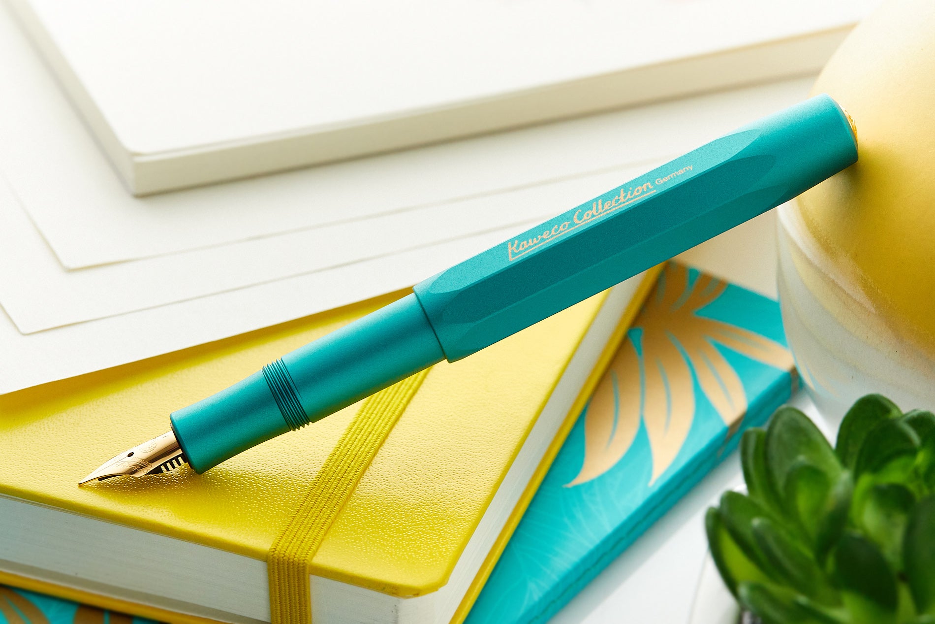 A teal Kaweco fountain pen on a yellow notebook