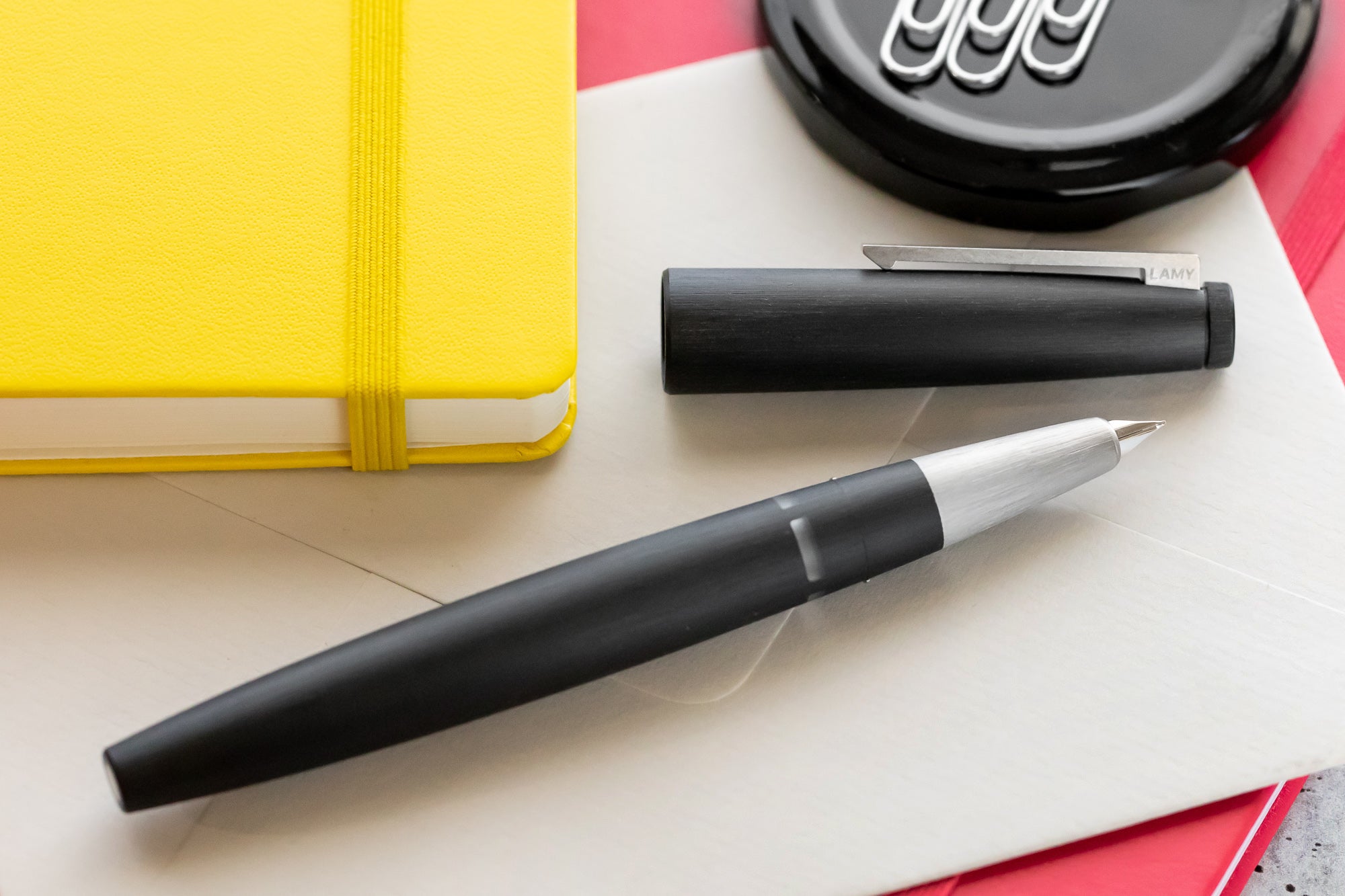 An open modern black fountain pen on a white envelope next to a yellow notebook