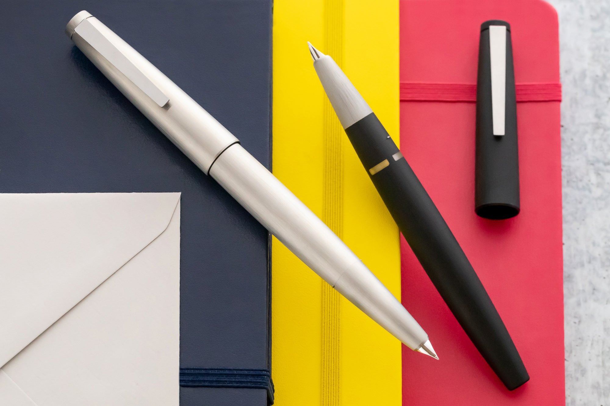 LAMY 2000 fountain pen in stainless steel finish, and black resin finish on blue, yellow and red notebooks