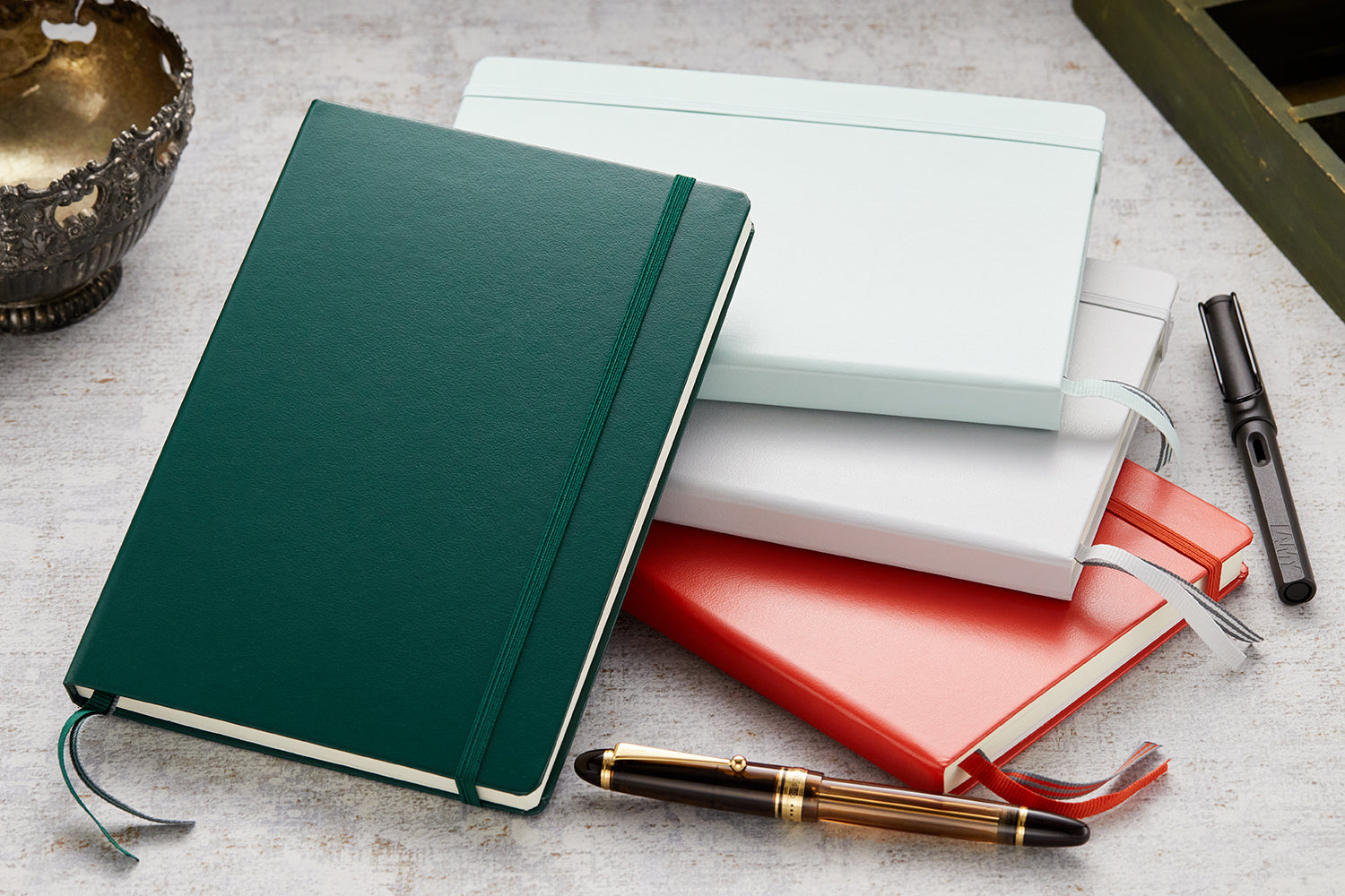 A stack of four notebooks with fountain pens