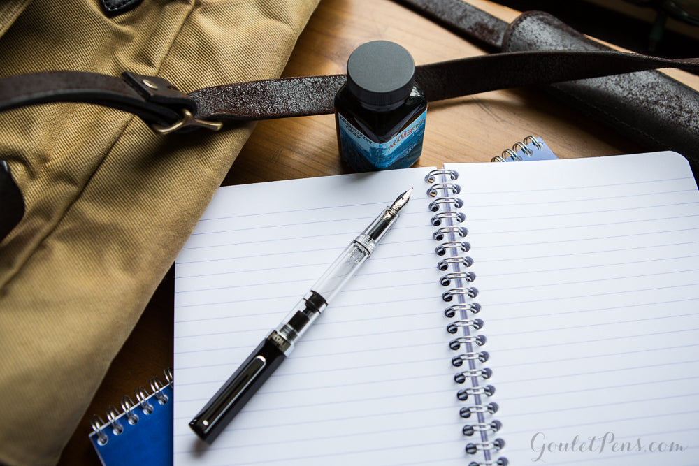 A black and clear fountain pen on top of an open lined wirebond notebook