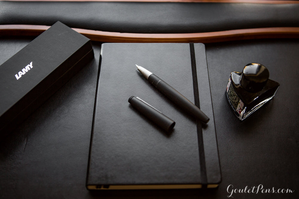 A modern black fountain pen on top of a closed black notebook