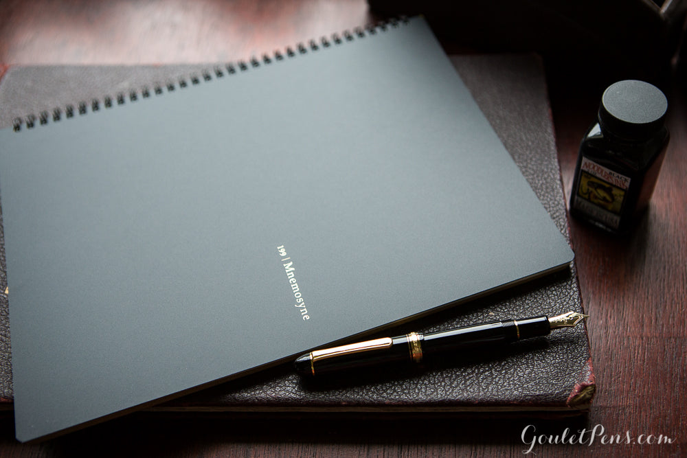 A large closed notebook next to a black and gold fountain pen