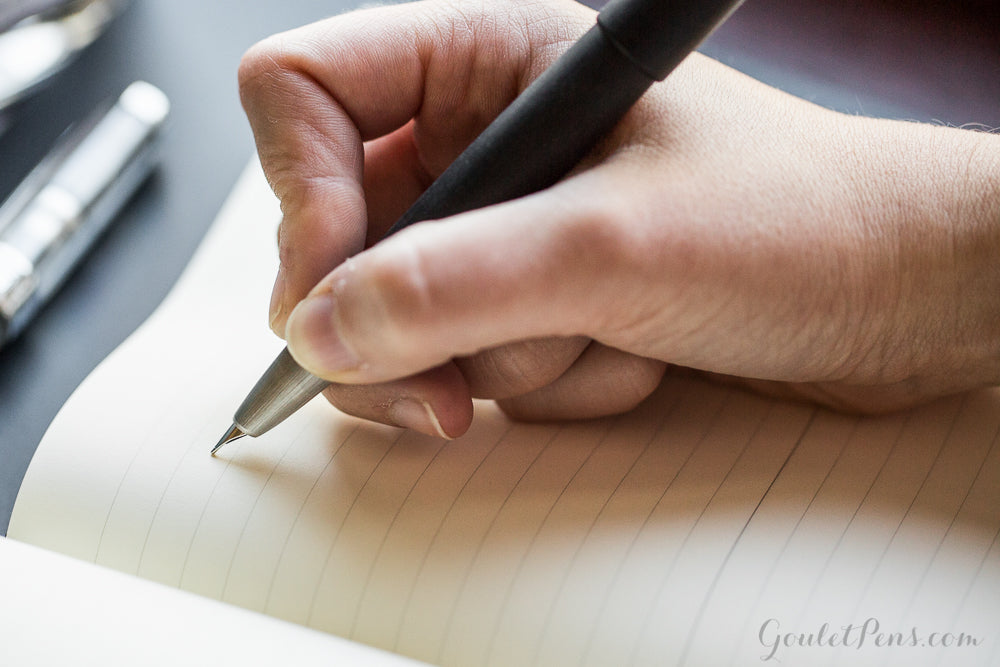 A hand holding a fountain pen about to write in a notebook