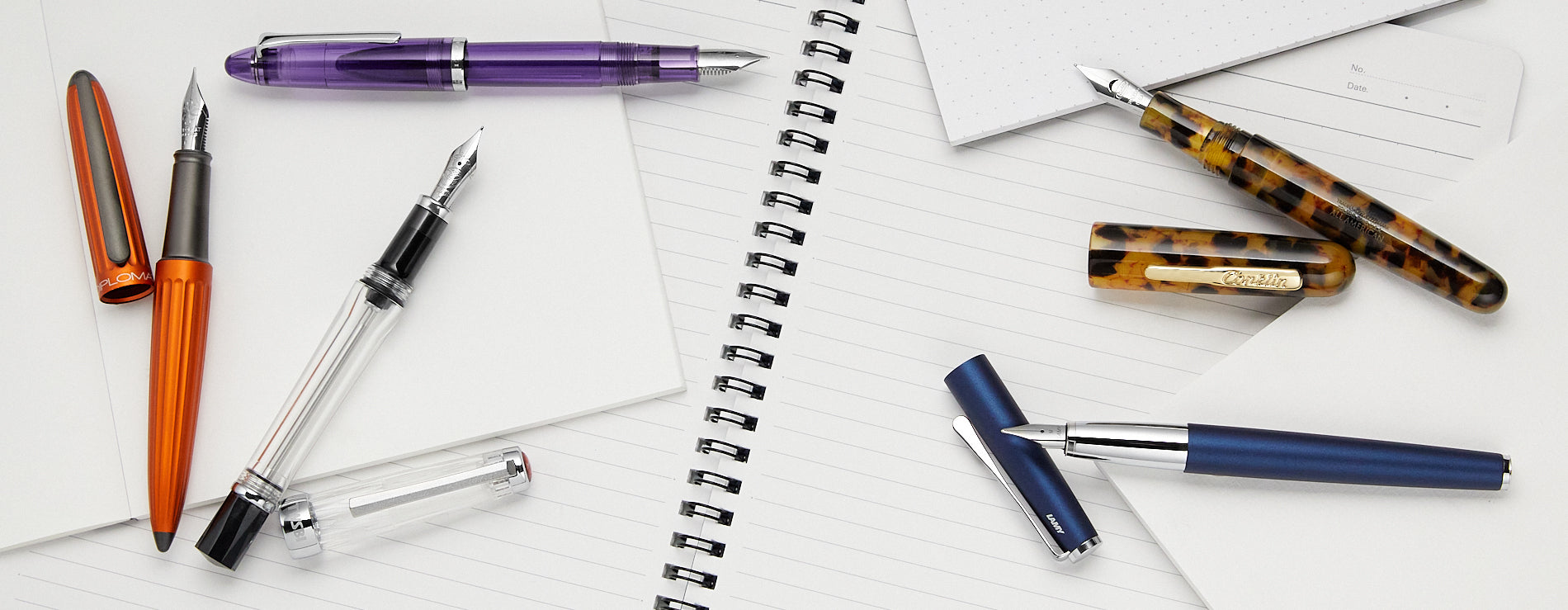 Several fountain pens scattered on an open wirebound notebook