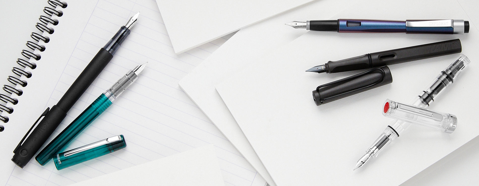 Several fountain pens scattered on top of white notebook paper