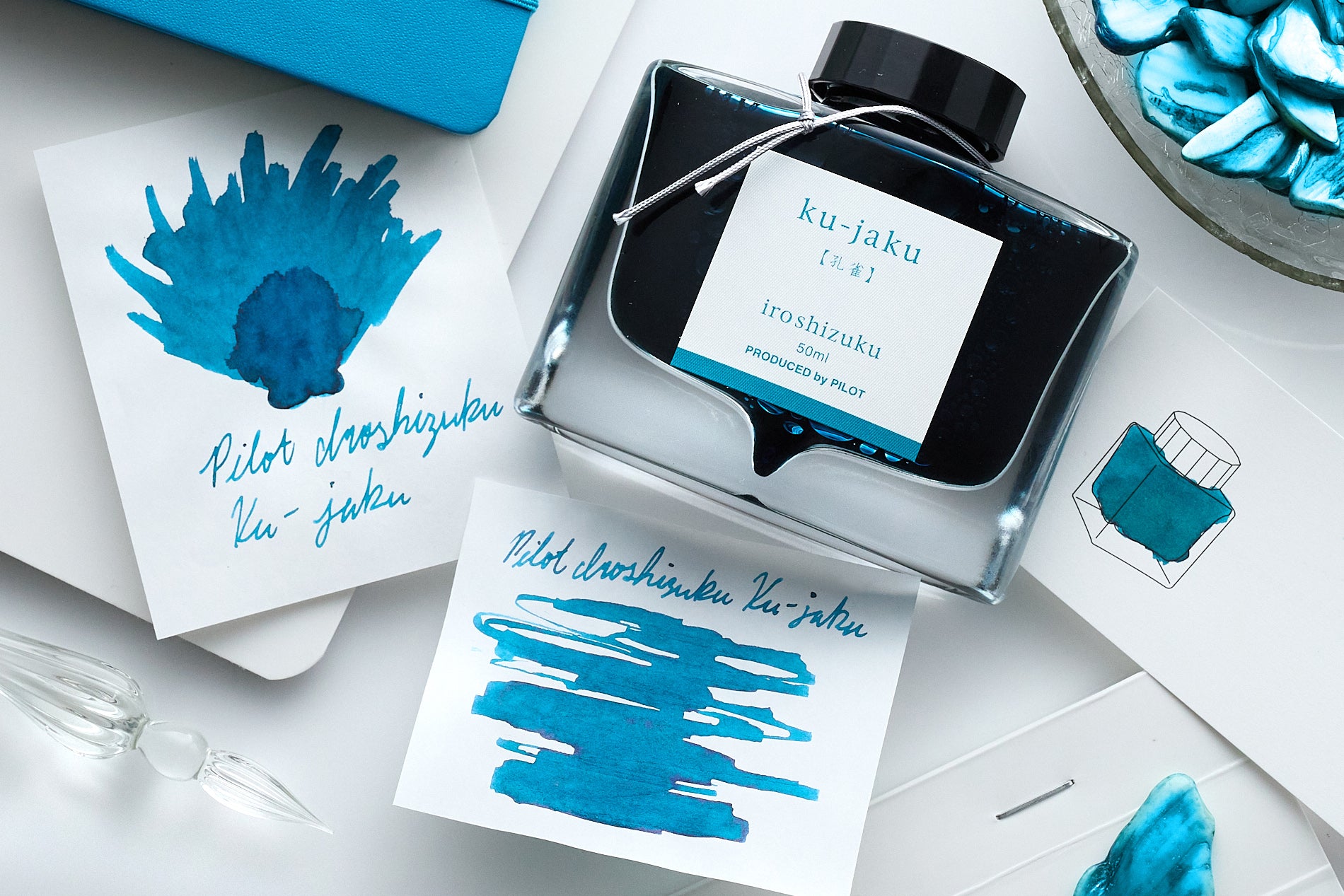 Pilot Iroshizuku Ku-Jaku Fountain Pen Ink writing sample, bottle and swabs on a white desk background with abalone shell pieces scattered about