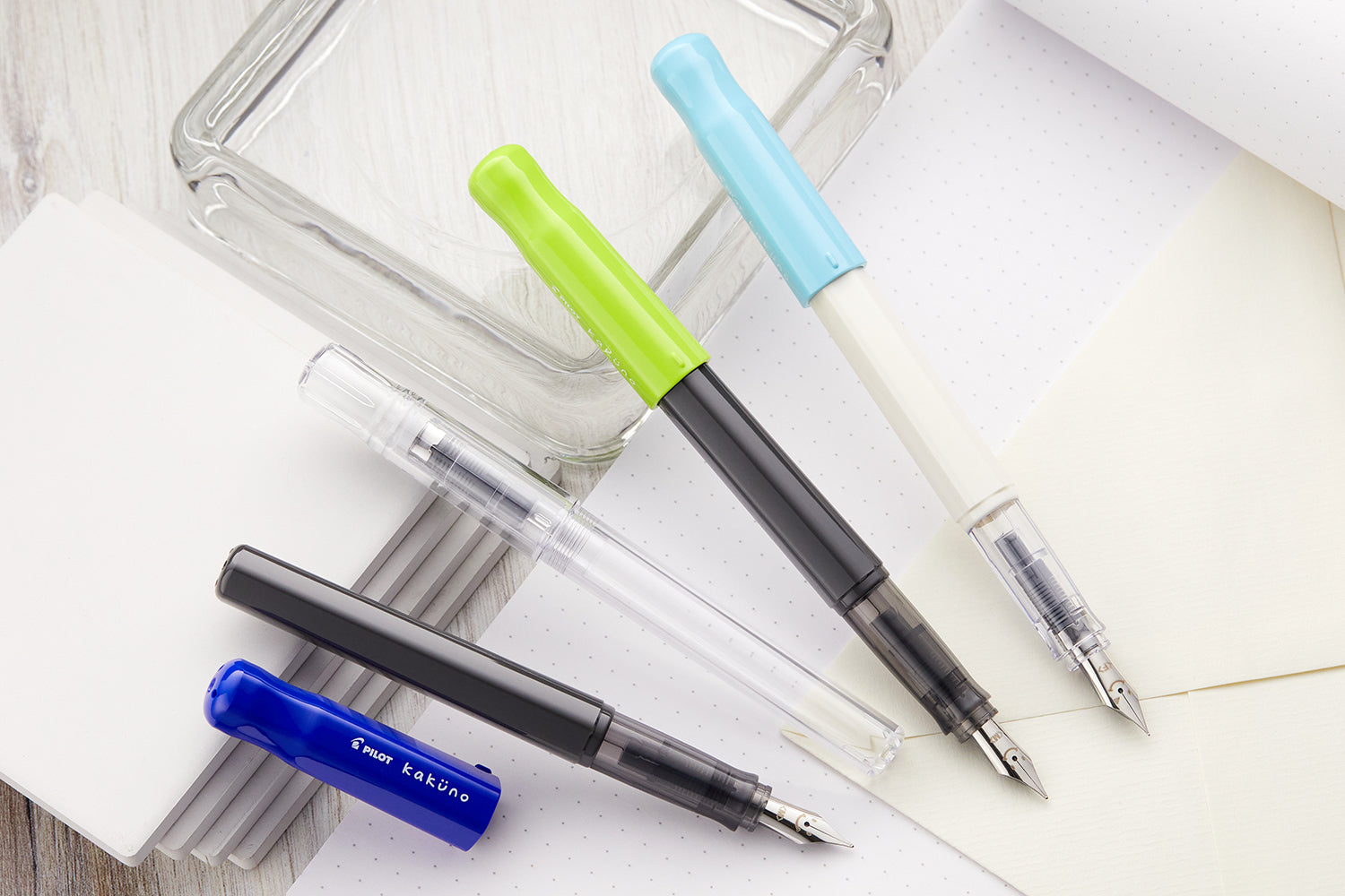 Four colorful fountain pens on top of open white notebooks