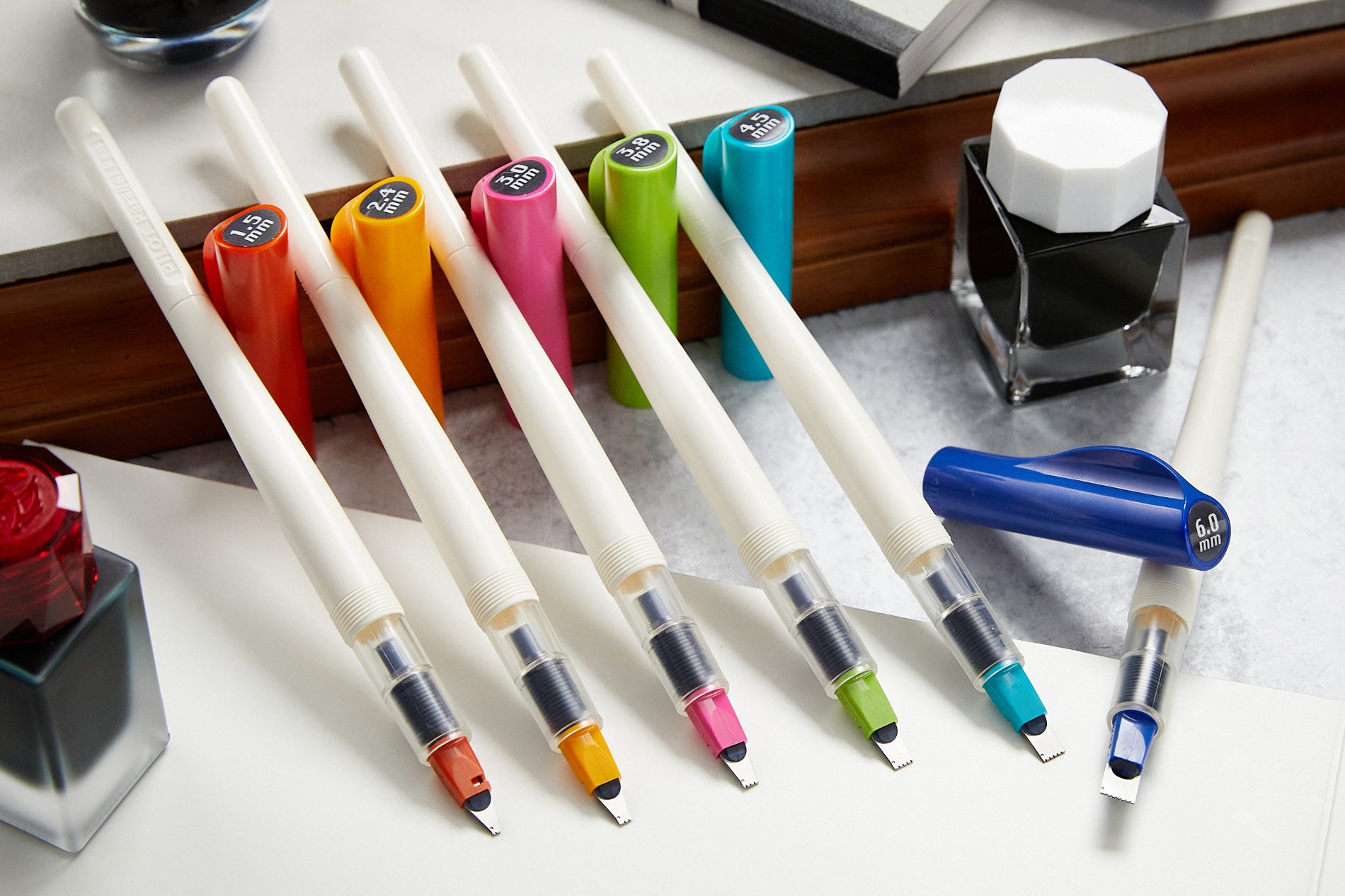 Six calligraphy-style fountain pens with white barrels and colorful caps, in a row