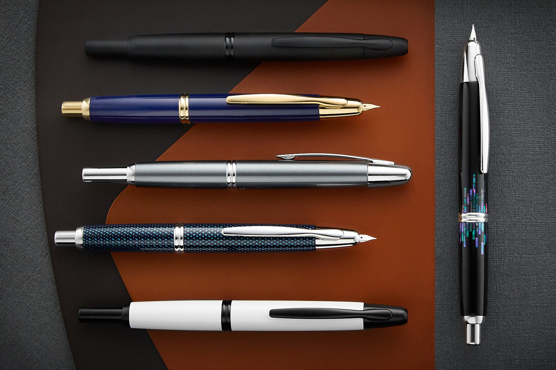 A group of retractable Pilot Vanishing Point fountain pens on a dark background