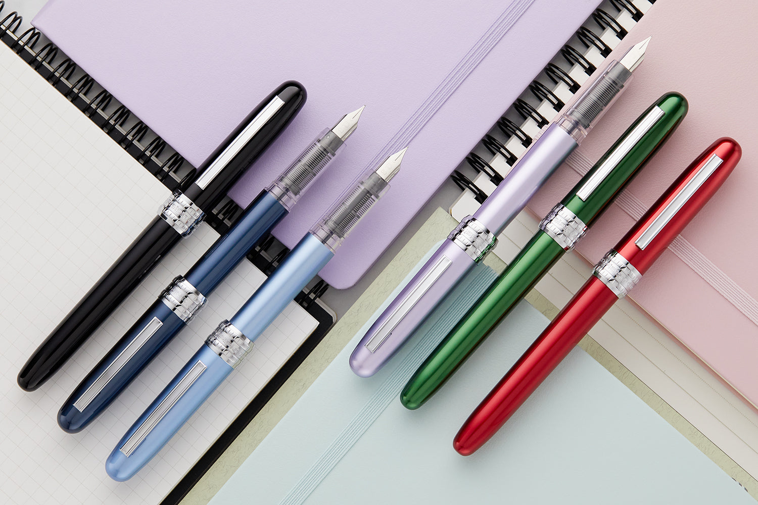 Several aluminum fountain pens lined up diagonally on top of notebooks