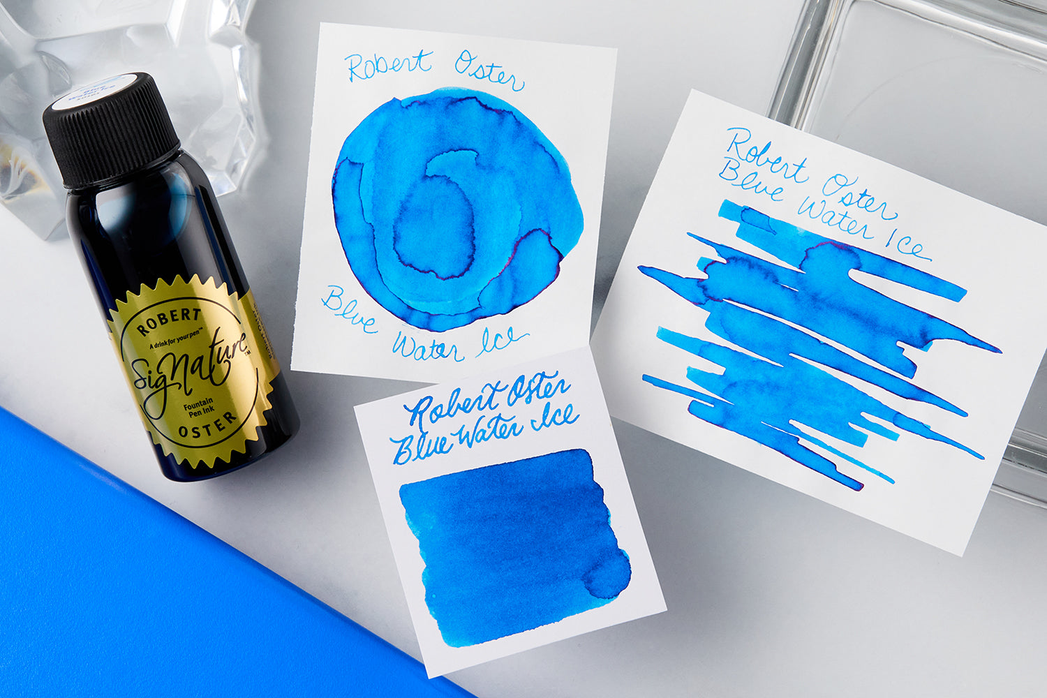 Robert Oster Blue Water Ice Fountain Pen Ink bottle, swab, swatch and additional swatch on white background