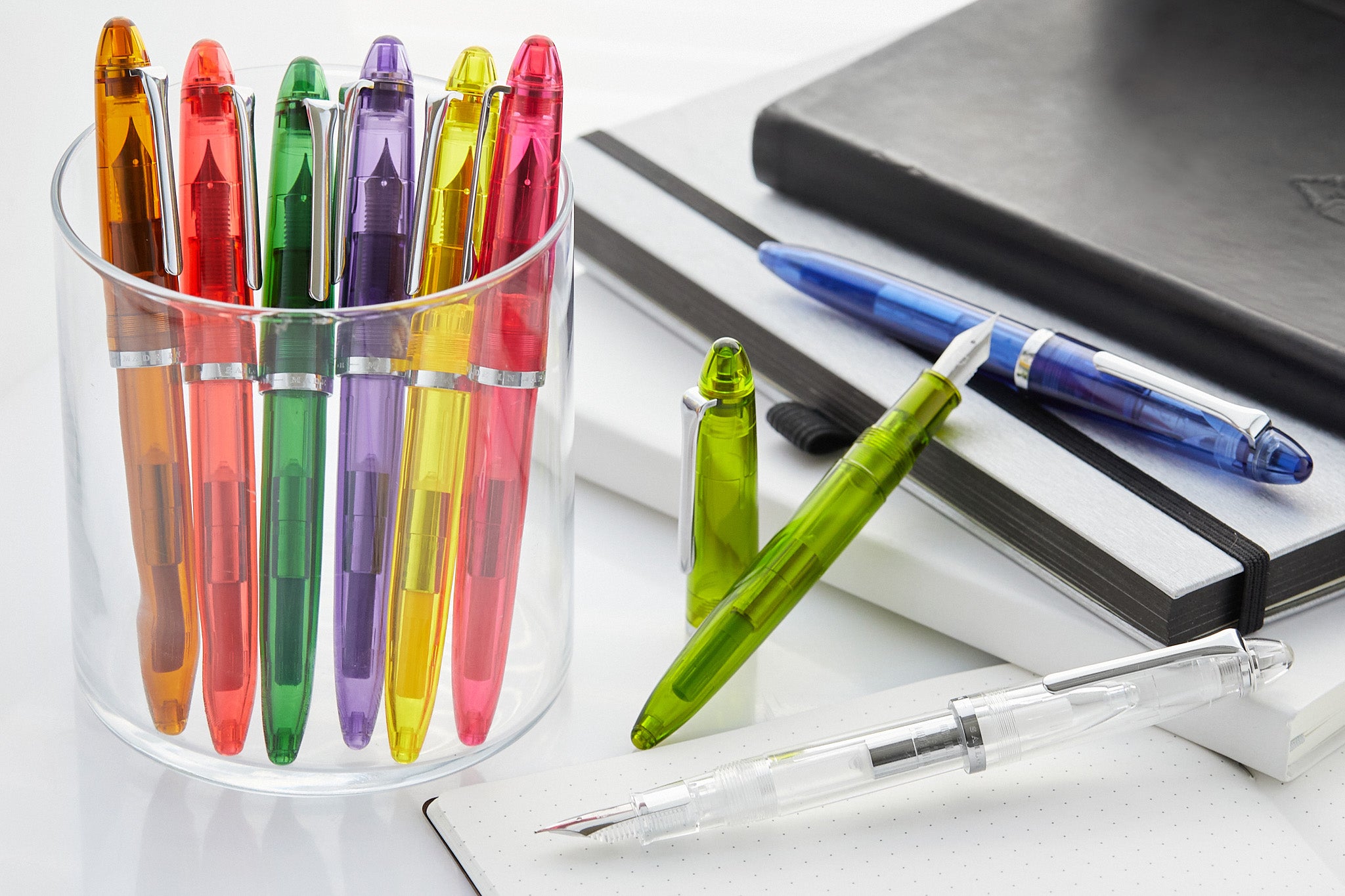 A rainbow of translucent resin fountain pens, some in a clear pen cup