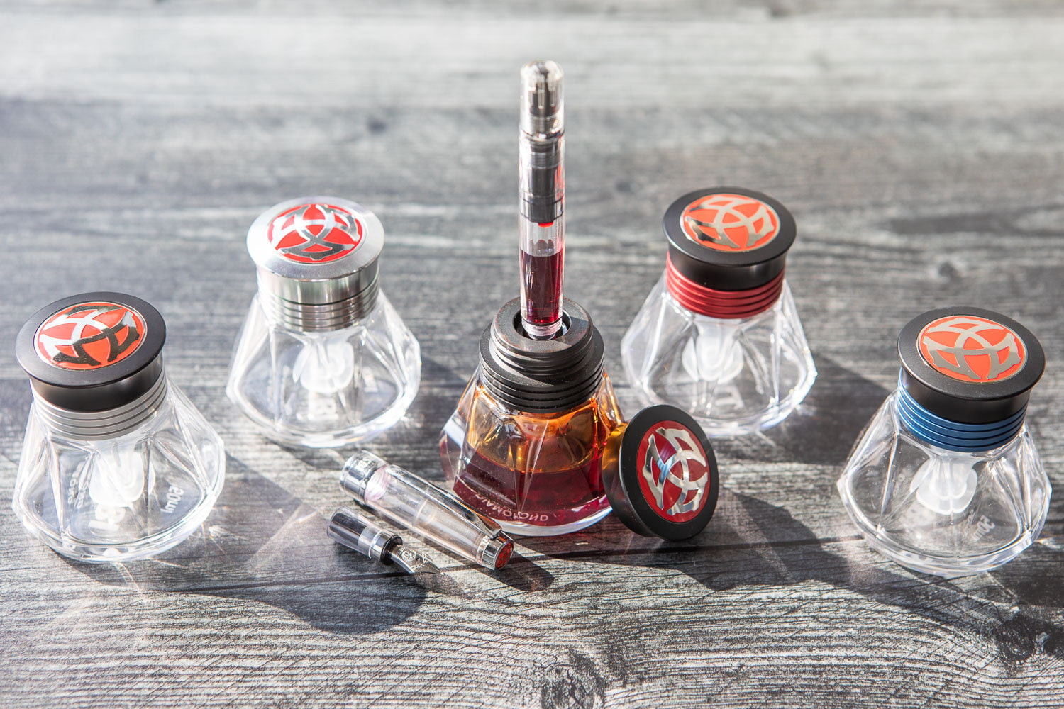 5 TWSBI Diamond 50 Inkwells with TWSBI Diamond pen in the middle one on grey wooden background