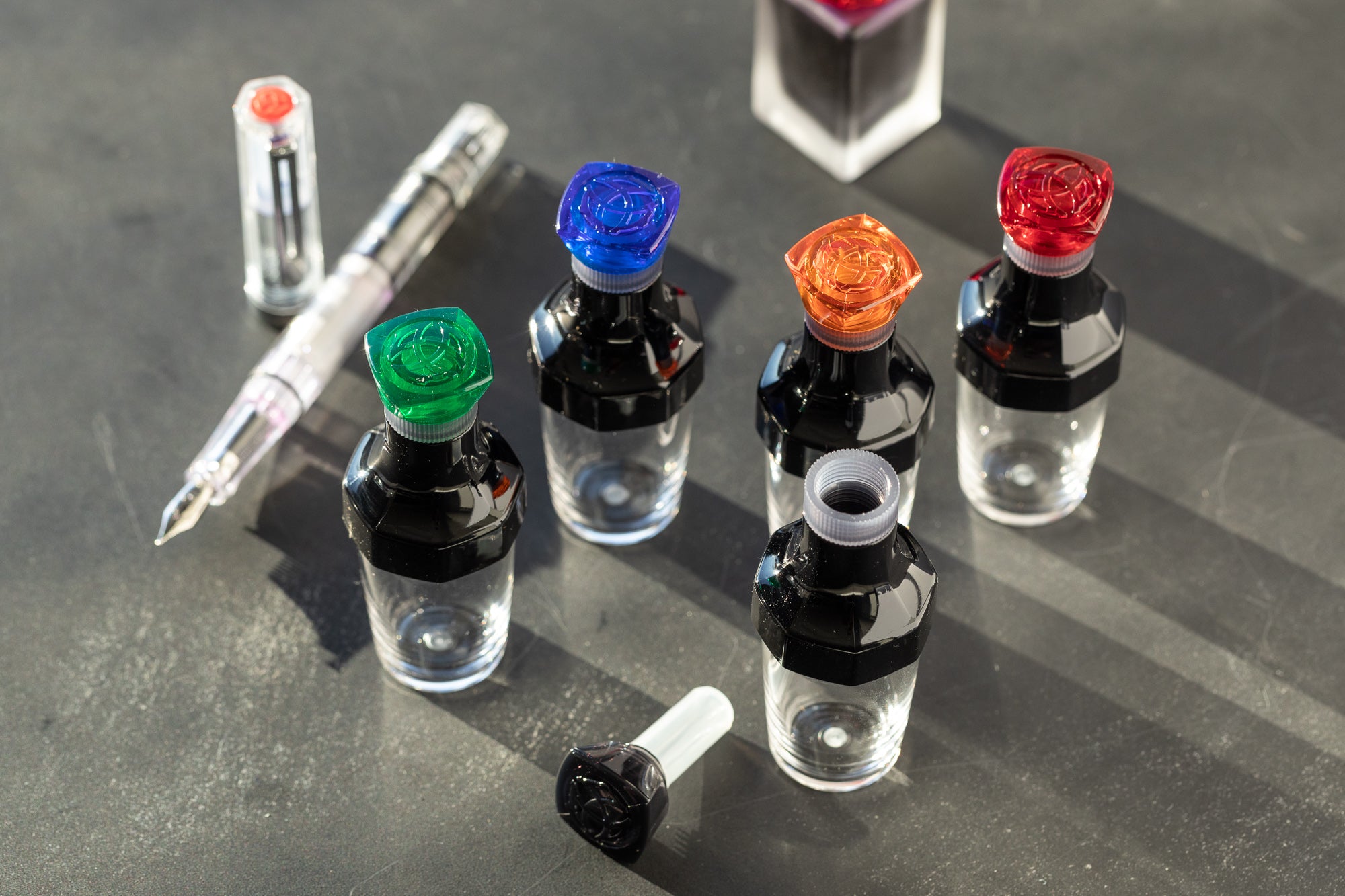 TWSBI Vac20 inkwells in assorted colors on gray desk background