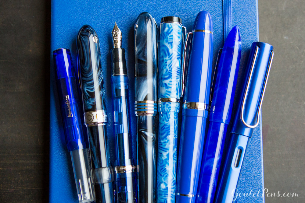 Assortment of blue fountain pens, capped and upcapped on blue journal