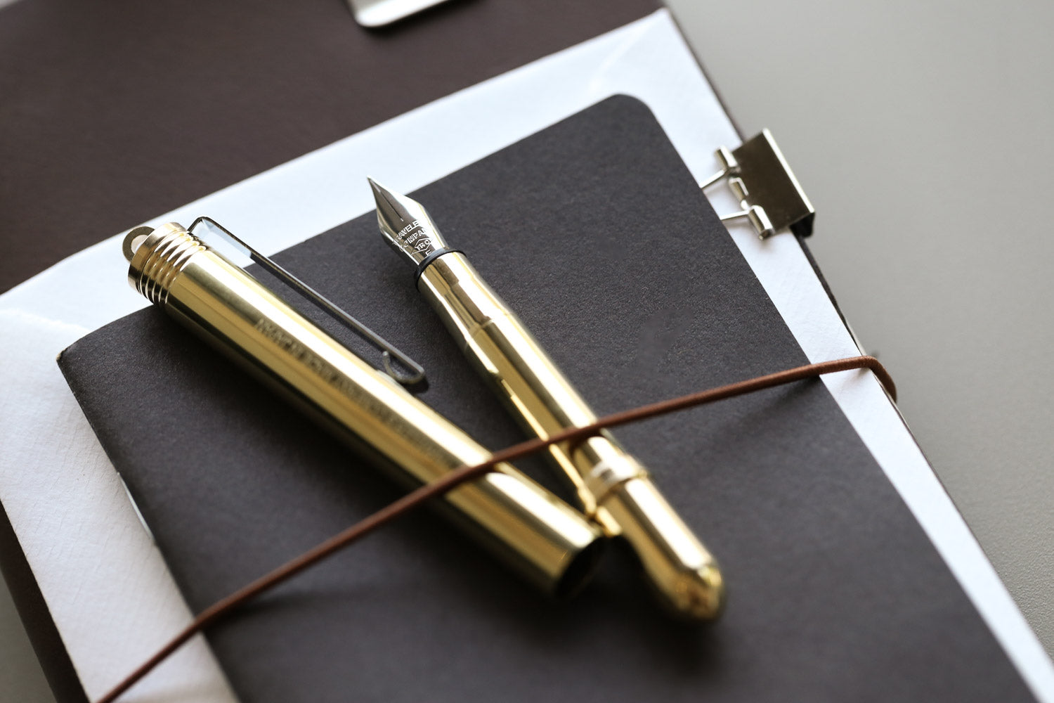 A small brass fountain pen tucked under the elastic strap on a brown leather notebook