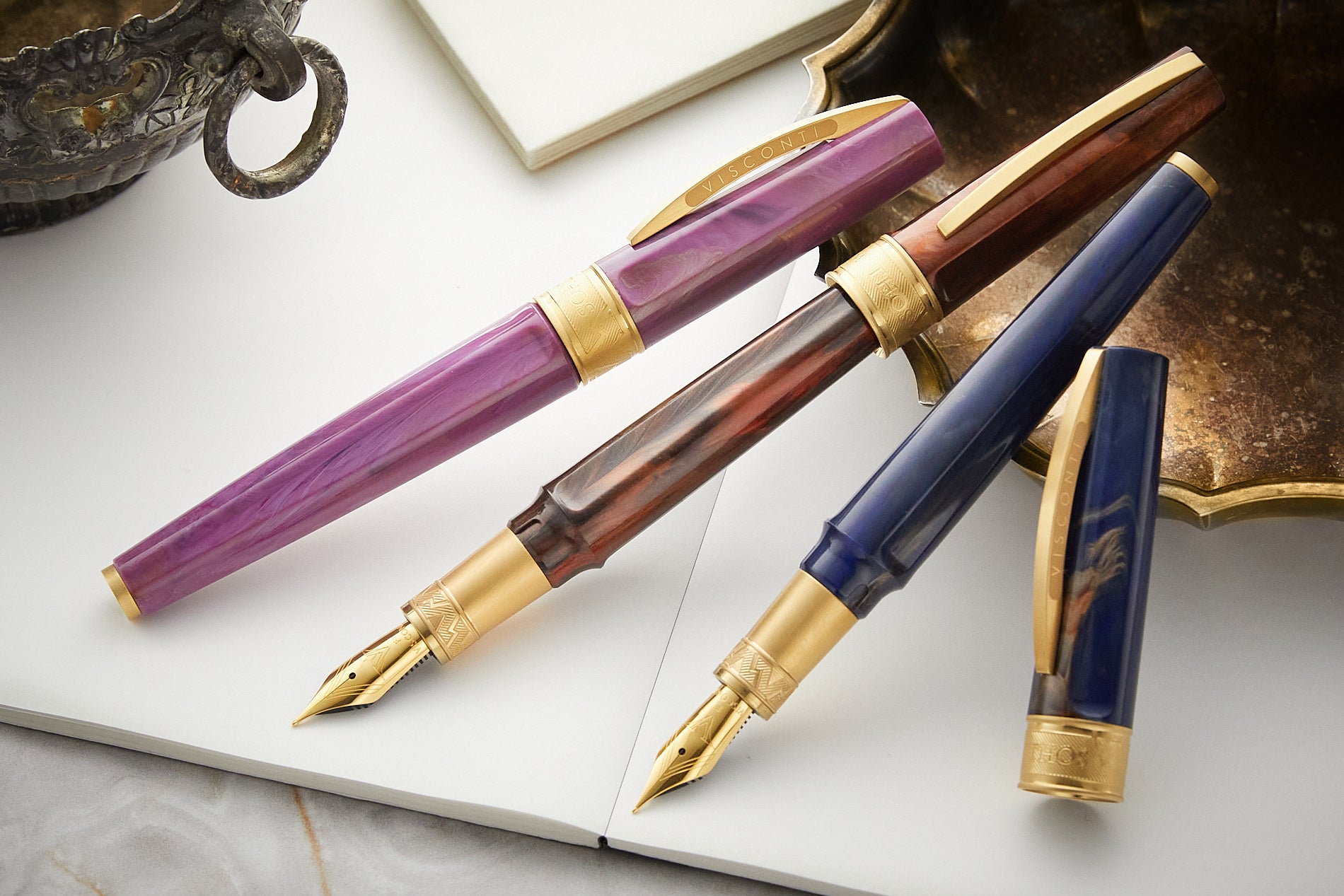 Visconti Mirage Mythos fountain pens in blue, brown and purple on white paper on top of a marble background