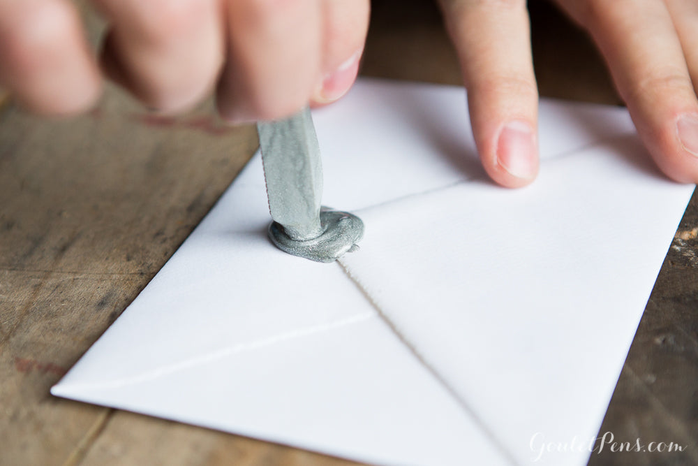 A hand pressing a melting stick of sealing wax onto paper