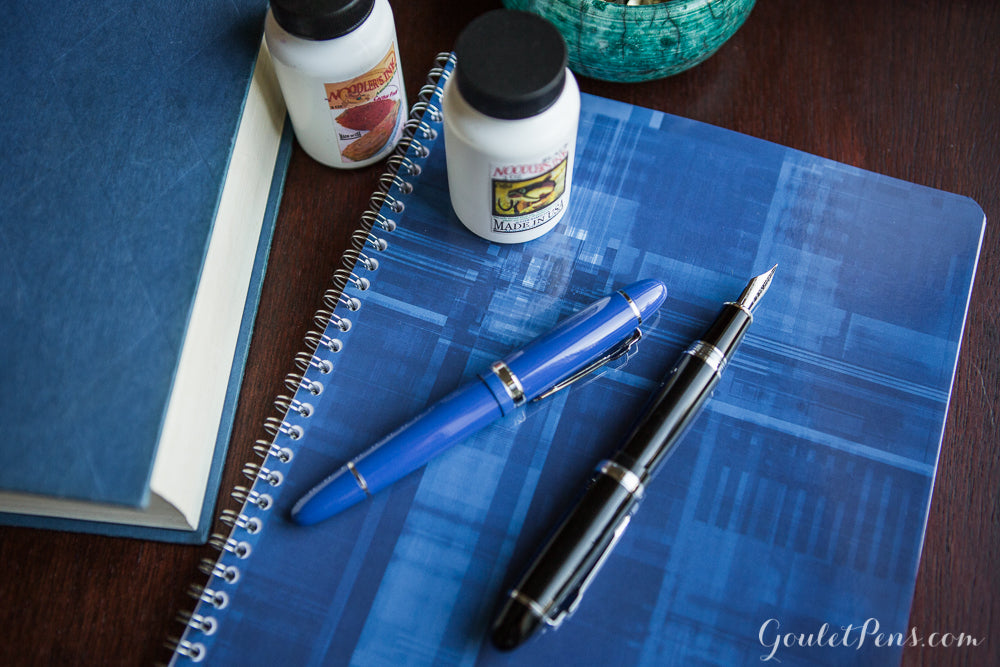 Jinhao fountain pen on top of blue notebook with ink bottles in the background