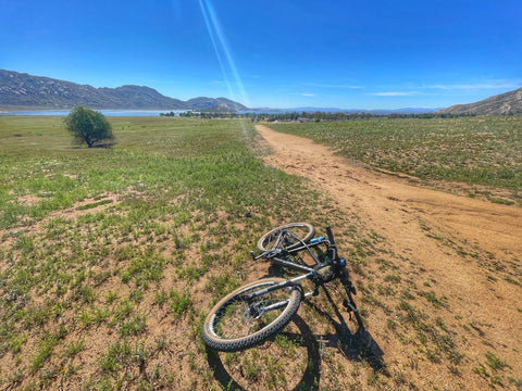 a bike on the ground by a dirt trail and a vista of a lake and mountains