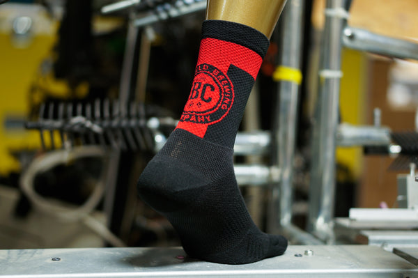 a black sock on a foot form showing a red brewery logo