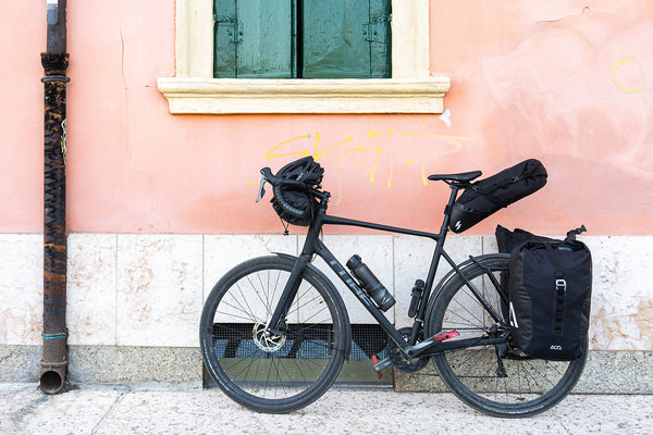a bike with packs over the wheel and on the handlebars leans against a pink wall