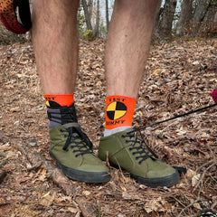 a man stands in the woods wearing green shoes and cycling socks with a red cuff featuring the crash test dummy logo