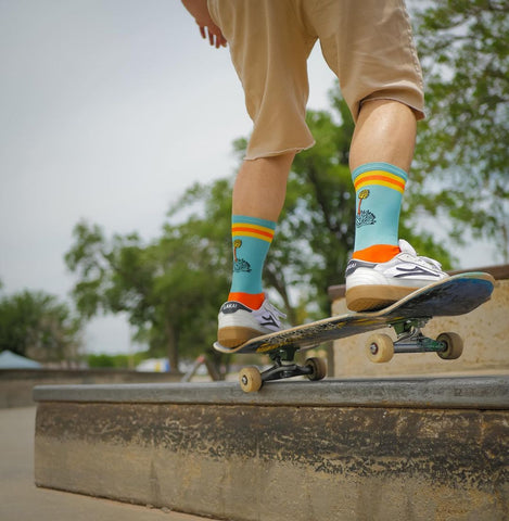 a man on a skateboard wearing brightly colored socks featuring the Pondaseta brewing logo