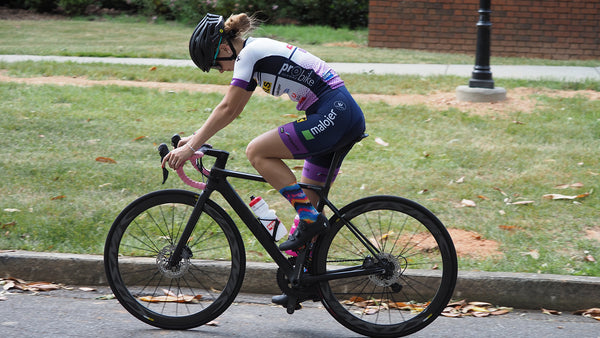 a young female cyclist riding on a paved road wearing DeFeet cycling socks