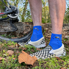 a man stands in the woods by his bike wearing black and white vans and blue cycling socks featuring a lone super sperm